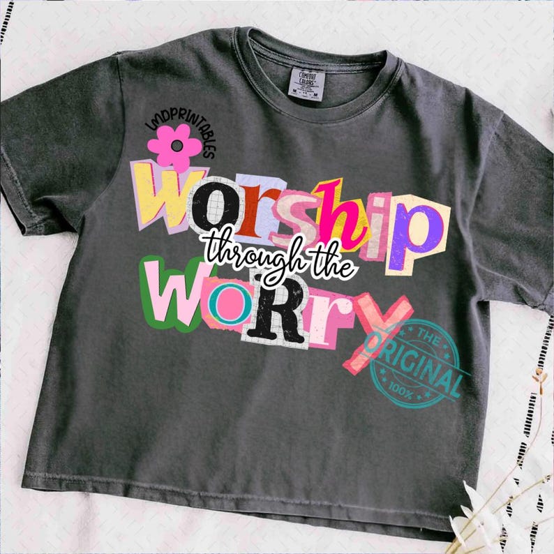 May include: Dark gray t-shirt with the words "Worship through the Worry" in a colorful, cut-out style. The shirt also features a pink flower graphic and a "The Original" stamp.