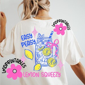 May include: Cream-coloured t-shirt with a colourful graphic design. The design features a mason jar filled with lemons and ice, with the words "Easy Peasy Lemon Squeezy". Pink flowers and text are also included.