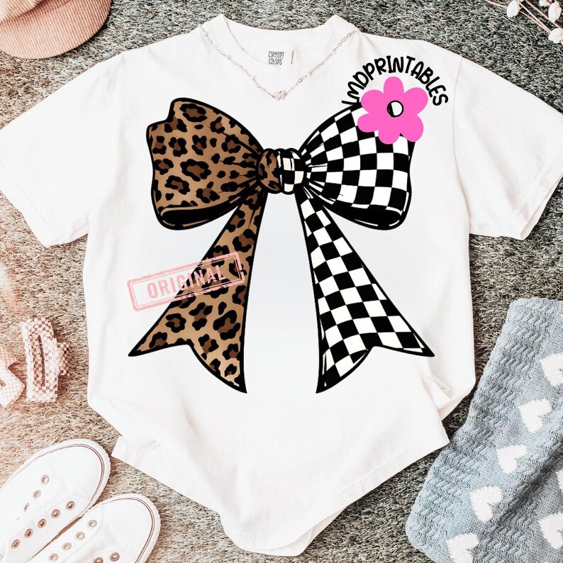 May include: White t-shirt featuring a large bow design. The bow has a leopard print on one side and a black and white checkered pattern on the other. A pink flower and the text "MDPRINTABLES" are above the bow.