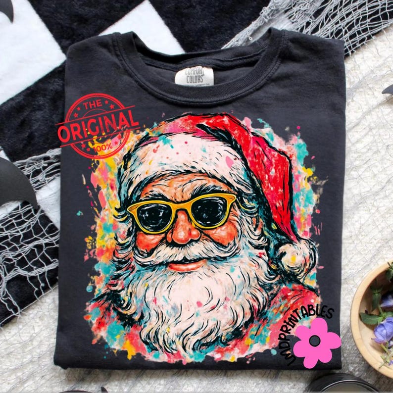 May include: Dark grey t-shirt with a colourful Santa Claus design. Santa wears yellow sunglasses and a red hat. The design includes the text "THE ORIGINAL" and "IMPRINTABLES".
