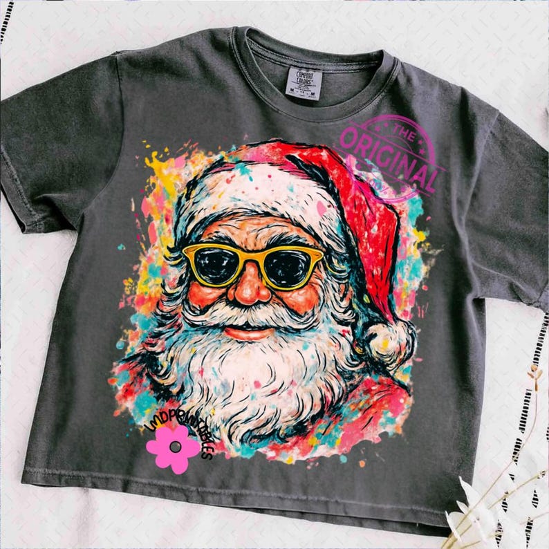 May include: Dark grey t-shirt with a colourful Santa Claus graphic. Santa is wearing yellow-framed sunglasses and a red hat. The graphic has a watercolour effect with the text "THE ORIGINAL" and a pink flower.