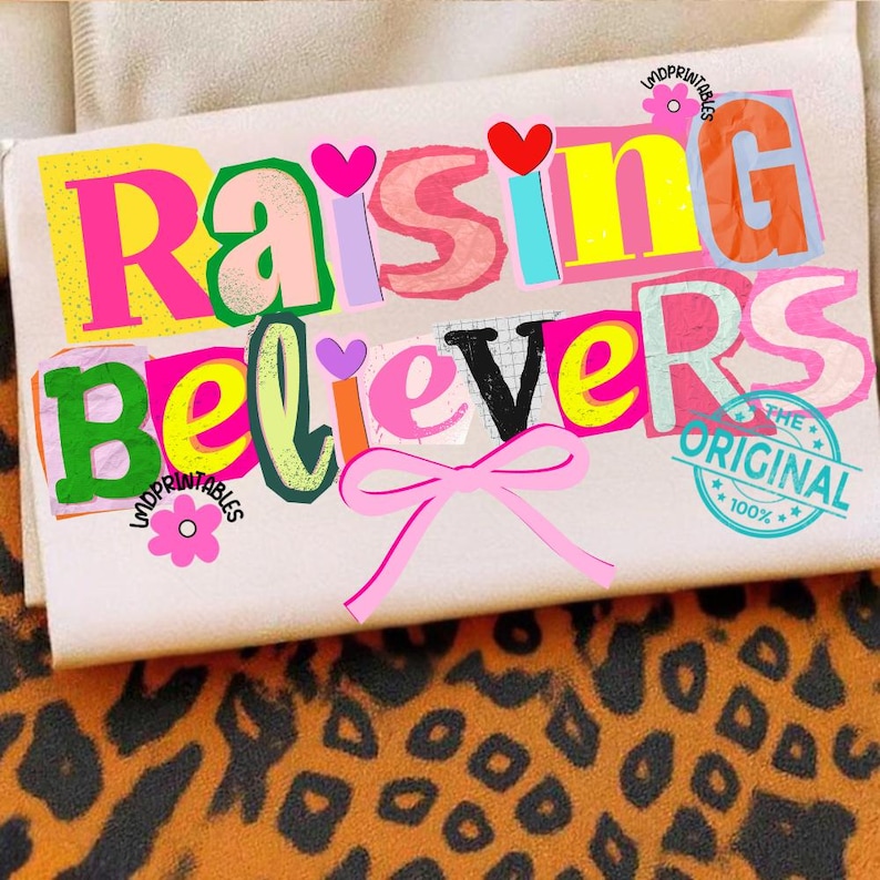 May include: A beige rectangular item with the words "Raising Believers" in colorful, layered text. The design includes hearts, a pink bow, and a circular stamp that reads "The Original 100%." The background features a leopard print.