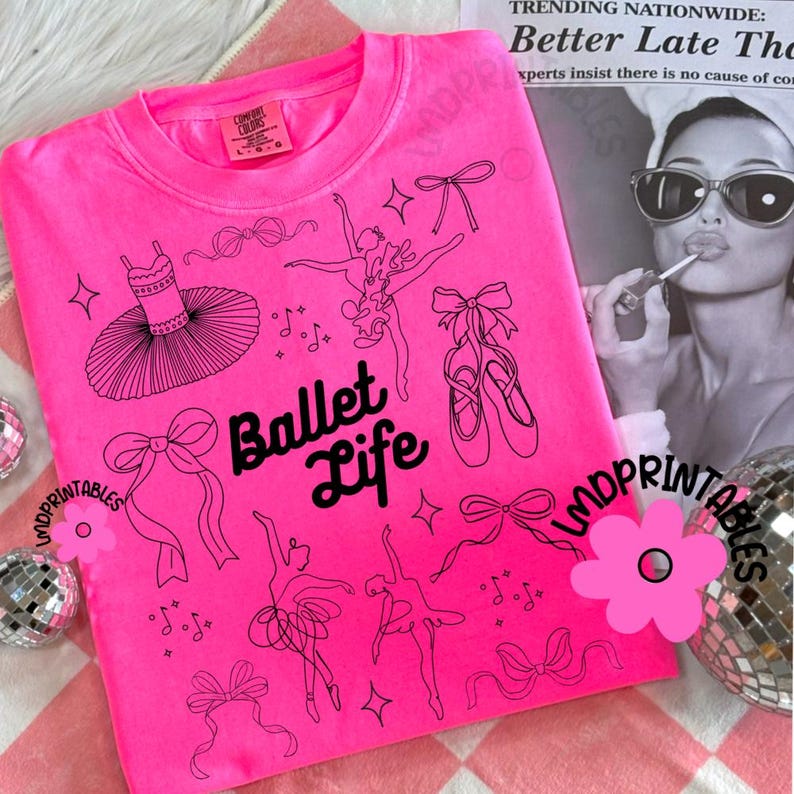 May include: A bright pink sweatshirt with the words "Ballet Life" and ballet-themed line art. The design includes a tutu, ballet shoes, bows, and dancing figures. The sweatshirt is a Comfort Colors brand.