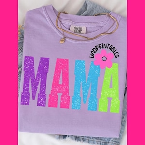 Pu&ograve; includere: Una maglietta lilla Comfort Colors con la scritta "MAMA" a grandi lettere colorate. Le lettere sono viola, rosa, blu e verdi. Visibile anche una collana d'oro e il testo "lmdprintables".