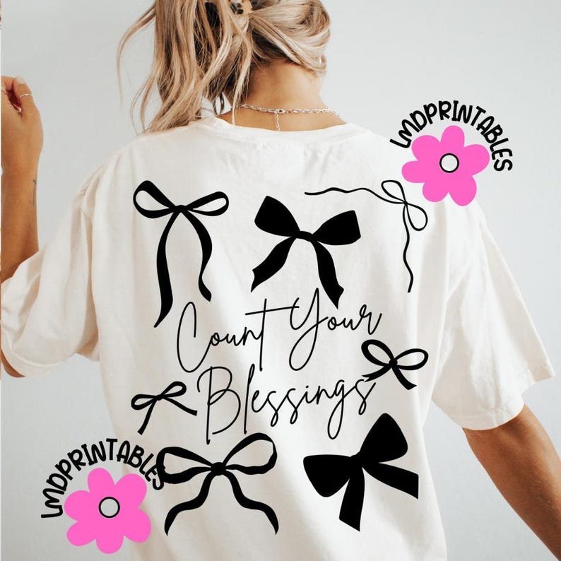 K&ouml;nnte beinhalten: Cremefarbenes T-Shirt mit schwarzen Schleifendesigns und dem handgeschriebenen Schriftzug "Count Your Blessings". Das Design umfasst verschiedene Schleifenstile und wird durch pinkfarbene Blumengrafiken mit dem Text "LMDPRINTABLES" akzentuiert.