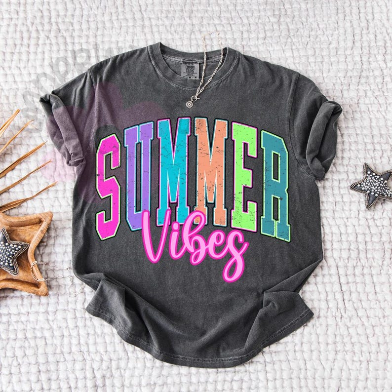 Puede incluir: Camiseta gris oscuro con la frase "SUMMER Vibes" en una fuente retro colorida. La palabra "SUMMER" est&aacute; en letras de bloque con un degradado de rosa, morado, azul, naranja y verde. "Vibes" est&aacute; en cursiva rosa.