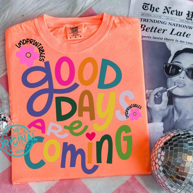 Może przedstawiać: Koralowa koszulka z napisem "GOOD DAYS ARE COMING" w kolorowych, zabawnych literach. Koszulka ma kwiatowy wz&oacute;r i napis "LMDPRINTABLES". Kula dyskotekowa i gazeta znajdują się w tle.