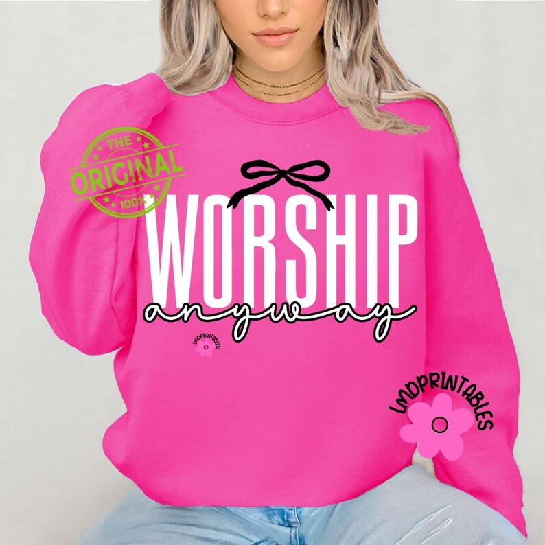 May include: A vibrant pink sweatshirt featuring the words "WORSHIP anyway" in white and black script. A black bow sits above "WORSHIP". The long-sleeved, crew-neck top has a stamp that says "THE ORIGINAL" on the left sleeve.