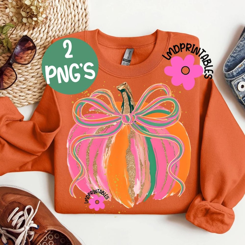 Peut inclure: Un sweat-shirt orange avec un motif de citrouille color&eacute;e orn&eacute; d'un n&oelig;ud rose et vert. La citrouille pr&eacute;sente des accents orange, rose et or. Le texte "2 PNG'S" est dans un cercle vert. Le texte "LMDPRINTABLES" est &eacute;galement visible.