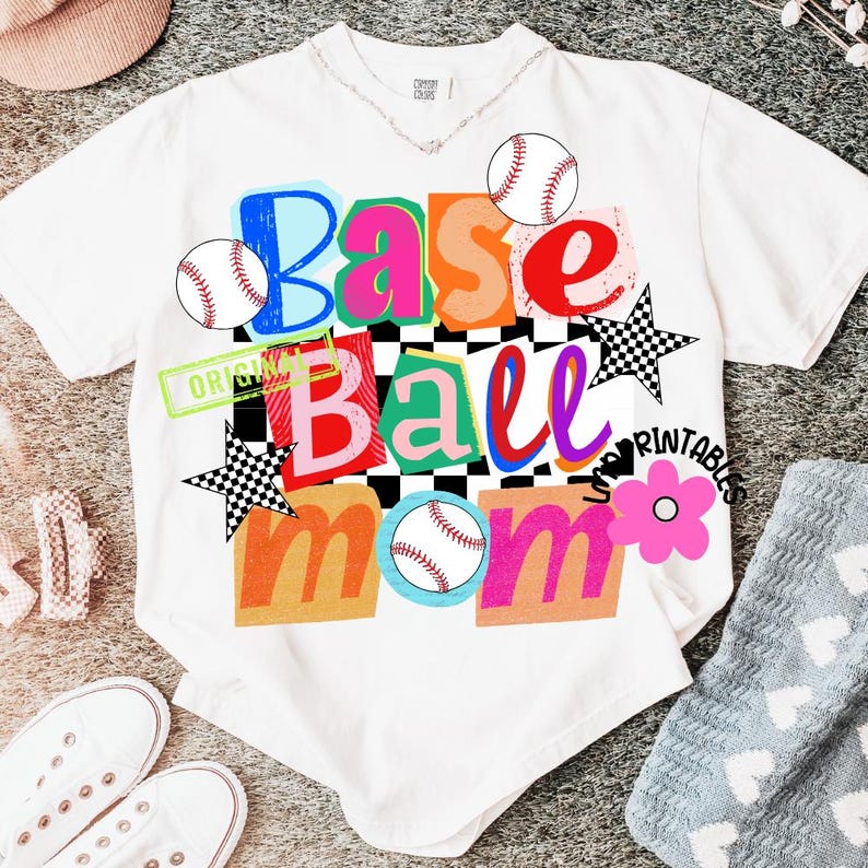以下が含まれることがあります： 「Base Ball Mom」と書かれたカラフルなグラフィックが特徴の白いTシャツ。デザインには野球ボール、星、花が含まれています。テキストはさまざまな色とフォントで、チェック柄の背景です。