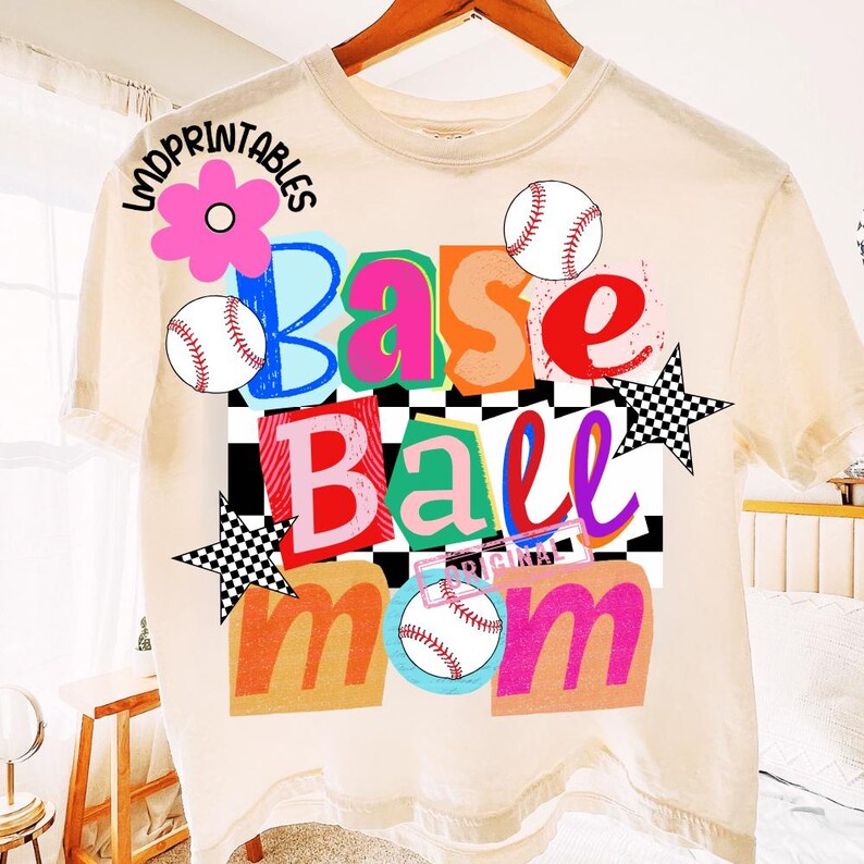 以下が含まれることがあります： 「Base Ball Mom」と書かれたカラフルなグラフィックが特徴のクリーム色のTシャツ。デザインには野球ボール、花、星の形が含まれています。テキストはさまざまな色とフォントで、白黒のチェック柄の背景です。