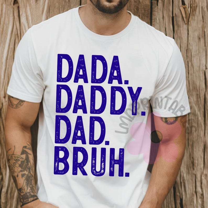 May include: White t-shirt with the words "DADA. DADDY. DAD. BRUH." printed in blue. The shirt is a crew neck style and appears to be made of cotton. The text is in a bold, sans-serif font.