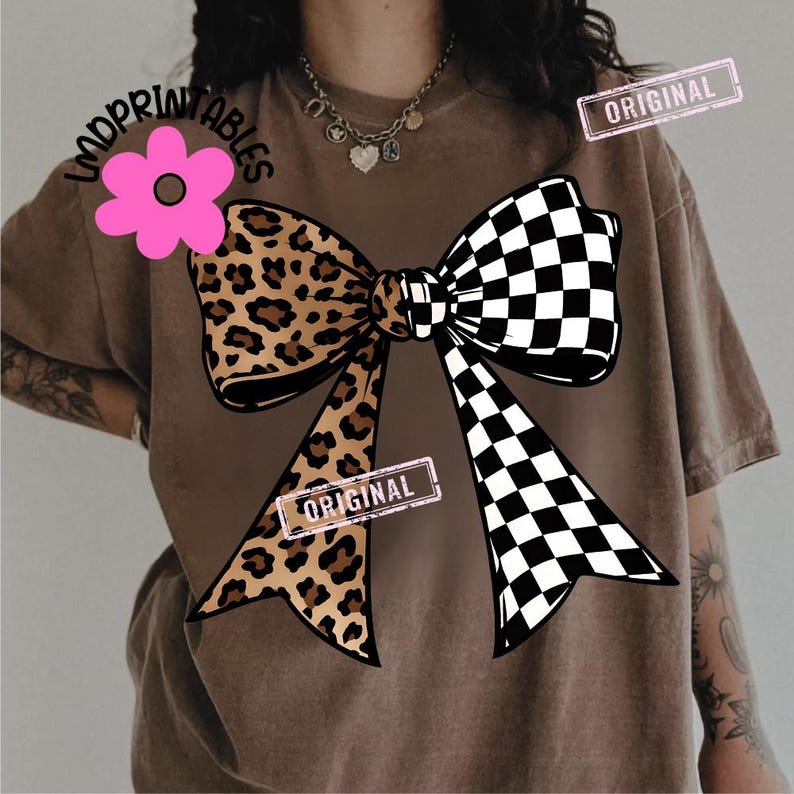 May include: Brown t-shirt featuring a large bow design. One side of the bow has a leopard print, while the other is a black and white checkerboard pattern. The shirt also has a pink flower graphic and the word "ORIGINAL" on it.