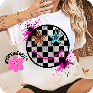 May include: White t-shirt with a black and white chequered smiley face design, featuring orange and turquoise star eyes. Pink and black paint splatters surround the smiley face. The text "LMDPRIINTABLES" is on the left side.