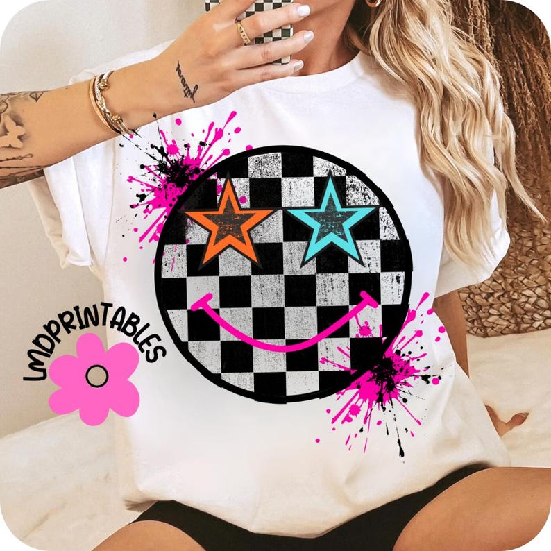 May include: White t-shirt with a black and white chequered smiley face design, featuring orange and turquoise star eyes. Pink and black paint splatters surround the smiley face. The text "LMDPRIINTABLES" is on the left side.