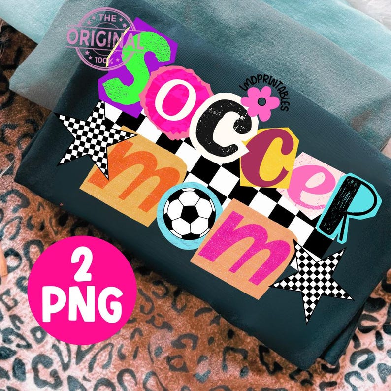 May include: Dark teal t-shirt with a colorful "Soccer Mom" graphic. The design includes a soccer ball, stars, and the text "2 PNG". The shirt is folded on a leopard print surface.