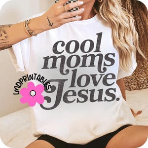 Puede incluir: Camiseta blanca con la frase "cool moms love Jesus" en gris oscuro, con un efecto desgastado. La camiseta tiene mangas cortas y cuello redondo. Un gr&aacute;fico de flor rosa con el texto "Lndprintables" est&aacute; en la esquina inferior izquierda.