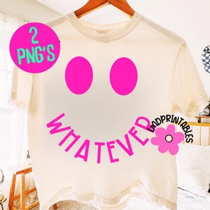 May include: Cream-colored t-shirt featuring a large, smiling face design. The face has two bright pink oval eyes and a curved "WHATEVER" smile in pink. A pink flower graphic and the text "LMDprintables" are on the right side.