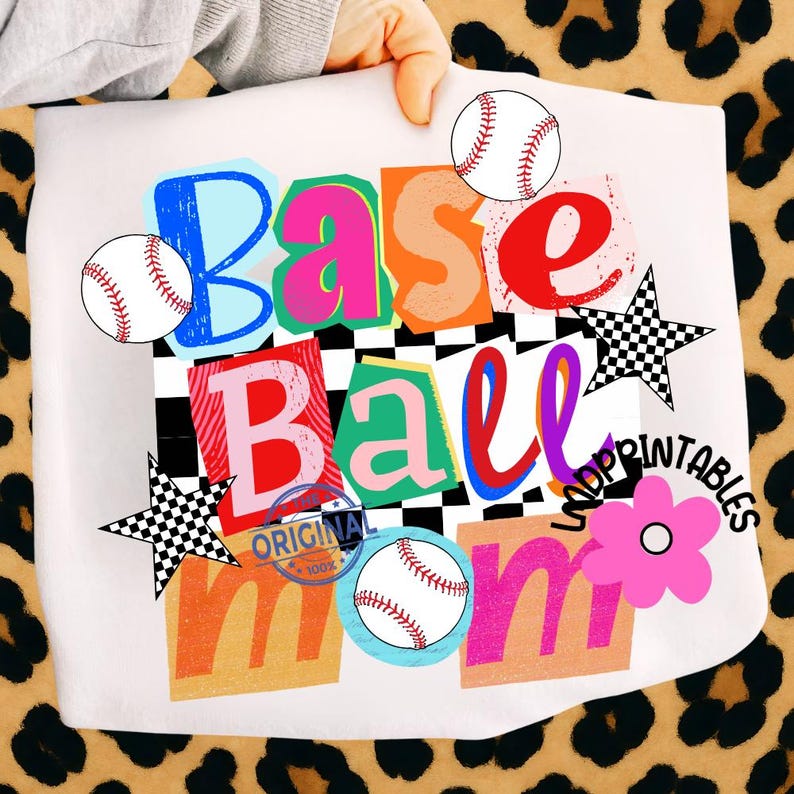 以下が含まれることがあります： カラフルなレイヤーテキストで「BASE BALL MOM」という言葉が書かれた白いグラフィック。野球のグラフィックと市松模様の星のアクセントがテキストを囲んでいます。ピンクの花と野球の青い円がデザインを完成させています。