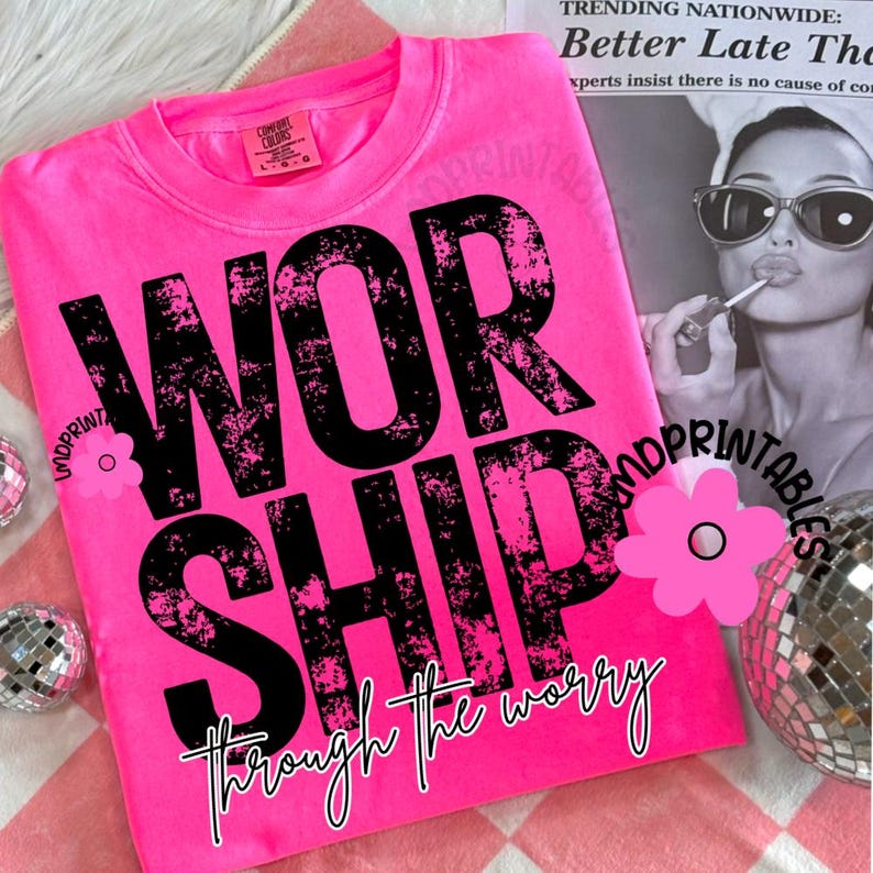 Pu&ograve; includere: Felpa rosa acceso con la parola "WORSHIP" in grandi lettere nere consumate. Sotto, la frase "through the worry" &egrave; scritta in un carattere script. La maglietta &egrave; su una superficie a scacchi rosa e bianca.