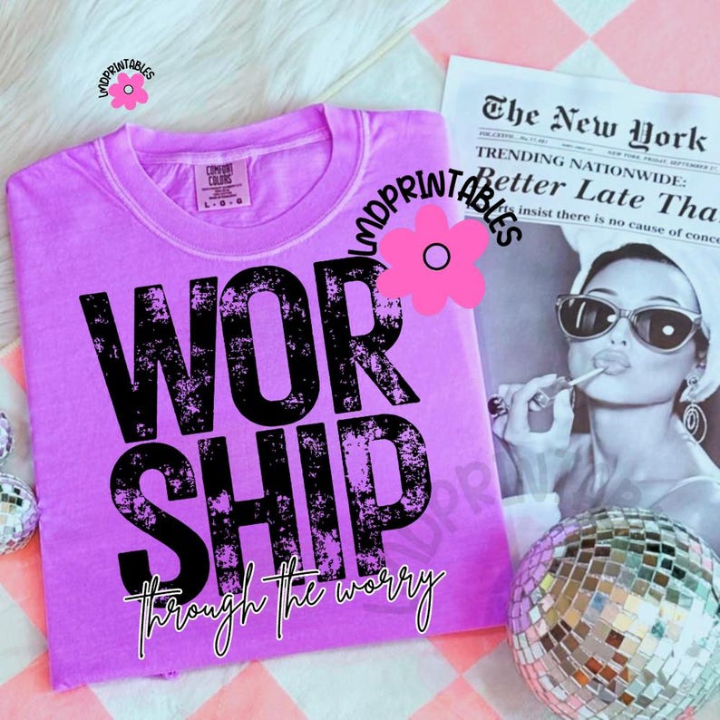 Pu&ograve; includere: Una maglietta lilla Comfort Colors con la scritta "WORSHIP" in lettere nere scolorite. Sotto la scritta c'&egrave; la frase "through the worry". Un ritaglio di giornale e una palla da discoteca sono sullo sfondo.