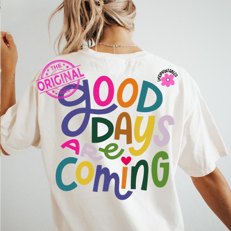 Może przedstawiać: Kremowa koszulka z napisem "Good Days Are Coming" w kolorowych, zabawnych literach. Projekt zawiera r&oacute;żową grafikę kwiatową i okrągłą pieczęć z napisem "The Original".