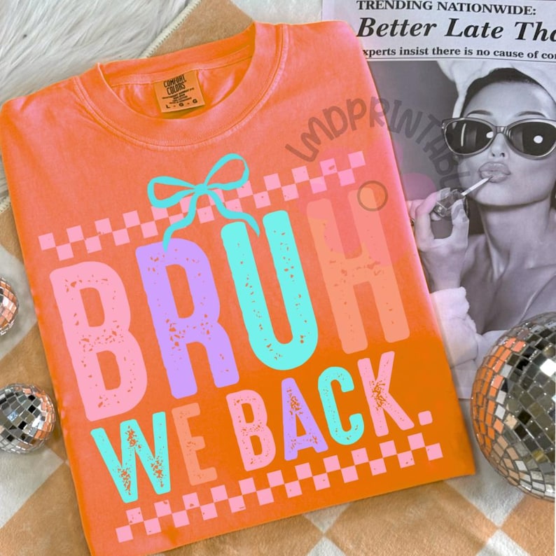 Puede incluir: Camiseta naranja Comfort Colors con el texto "BRUH WE BACK" en una fuente retro colorida. El dise&ntilde;o incluye un lazo y patrones de cuadros. La camiseta se muestra sobre una superficie estampada con bolas de discoteca.