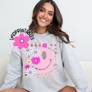Op de afbeelding: Een lichtgrijs sweatshirt met een roze smiley-gezichtontwerp, versierd met madeliefjes en andere bloemen. Het smiley-gezicht staat tegen een roze en witte geblokte achtergrond. De tekst "LMDPRINTABLES" staat in de linkerbovenhoek.