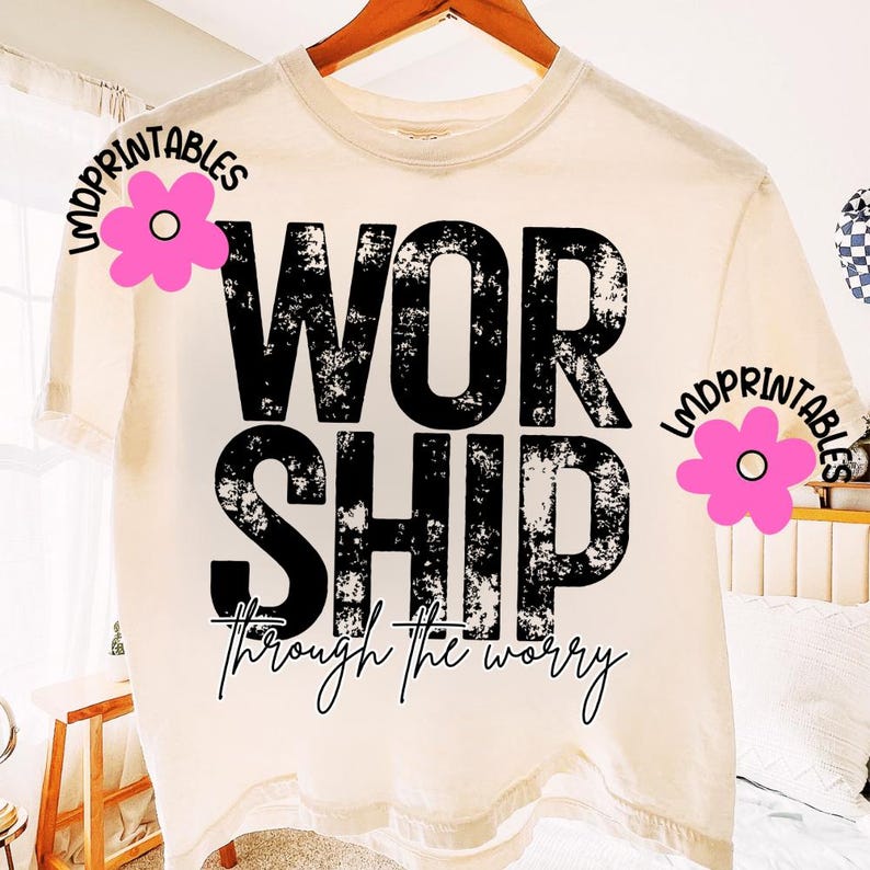 Pu&ograve; includere: T-shirt color crema con la scritta "WORSHIP" in grandi lettere nere sbiadite. Sotto, la frase "through the worry" &egrave; scritta in un carattere corsivo. La maglietta &egrave; appesa a una gruccia di legno.