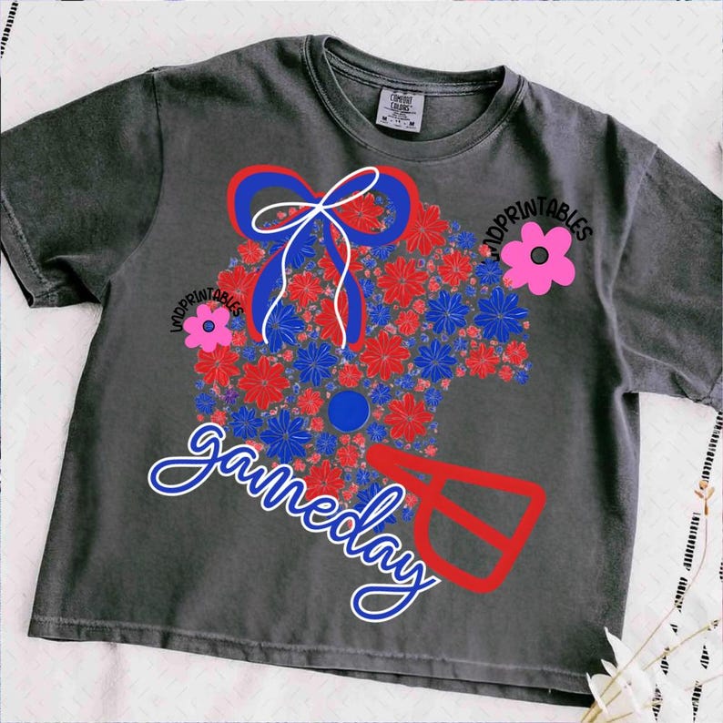 May include: Dark gray t-shirt with a floral design in red, blue, and white, featuring the word "gameday" in a script font. The design includes a bow and a football helmet shape. The text "IMDPRINTABLES" is also visible.