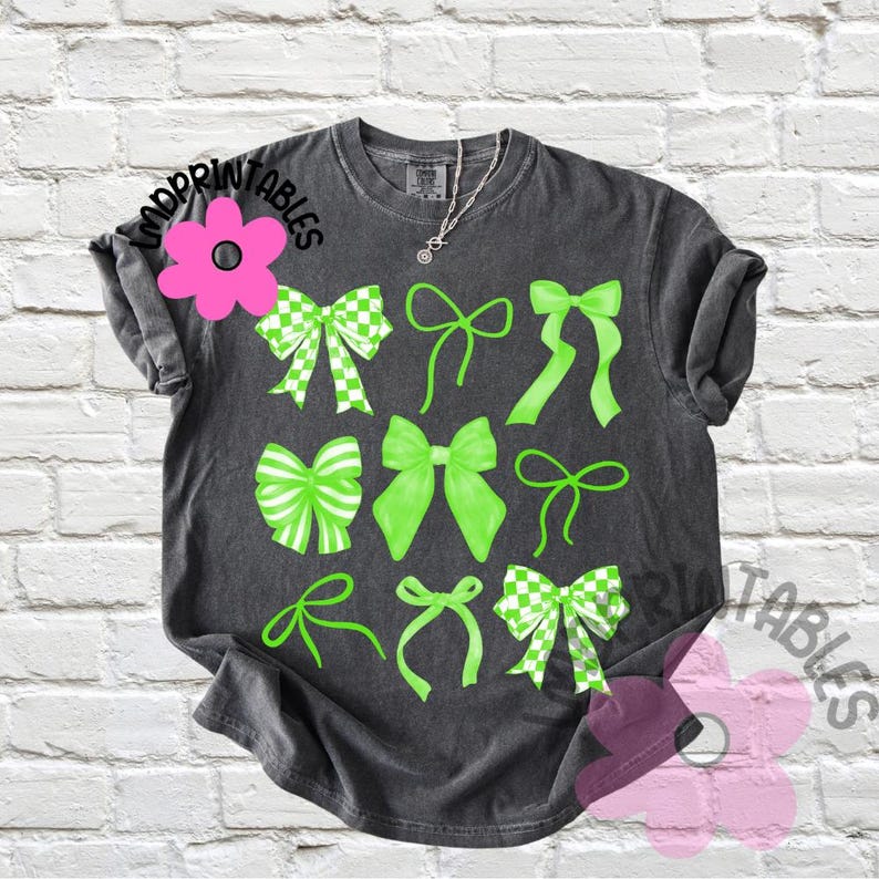 May include: Dark gray t-shirt featuring a collection of green bows in various styles. Some bows have a checkered pattern. The shirt has the text "Printables" in a floral design.