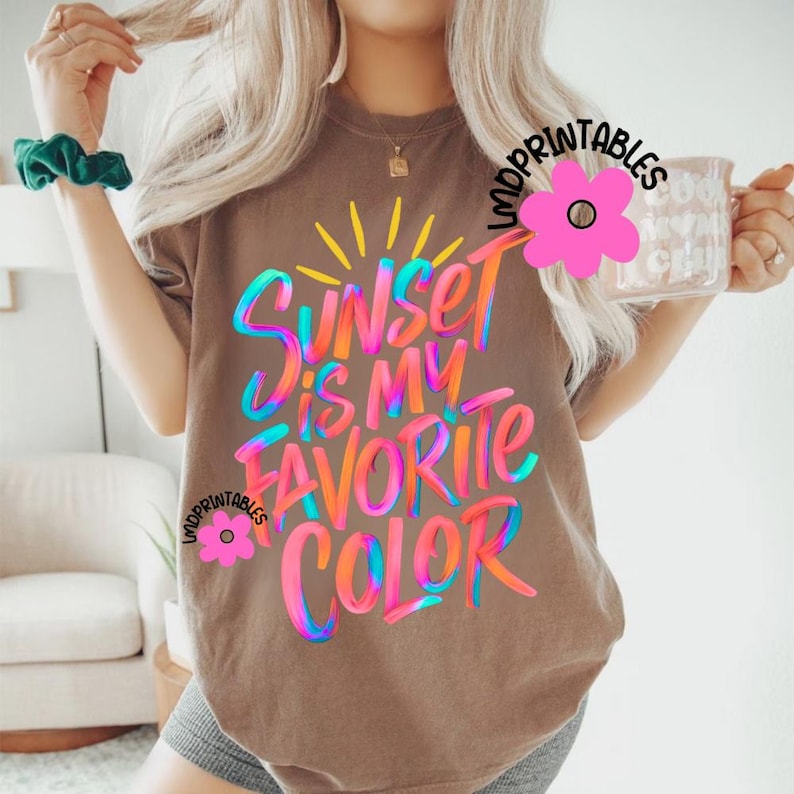May include: A brown t-shirt with the text "Sunset is my favorite color" in colorful, stylized lettering. The design includes a yellow sunburst and the words are in shades of blue, pink, orange, and green.