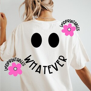 May include: Cream-colored t-shirt with a large black smiley face design. The design includes two black oval eyes and the word "WHATEVER" in a curved font. Pink flower graphics with the text "LMDPRINTABLES" are also present.