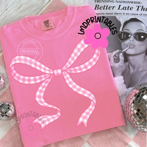 May include: A pink Comfort Colors sweatshirt featuring a large gingham bow design. The bow is white and pink. The text "ORIGINAL" is printed on the shirt. The text "LMDPRINTABLES" is printed on the shirt. A pink flower is on the shirt.