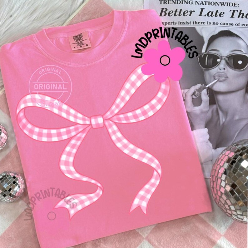 May include: A pink Comfort Colors sweatshirt featuring a large gingham bow design. The bow is white and pink. The text "ORIGINAL" is printed on the shirt. The text "LMDPRINTABLES" is printed on the shirt. A pink flower is on the shirt.