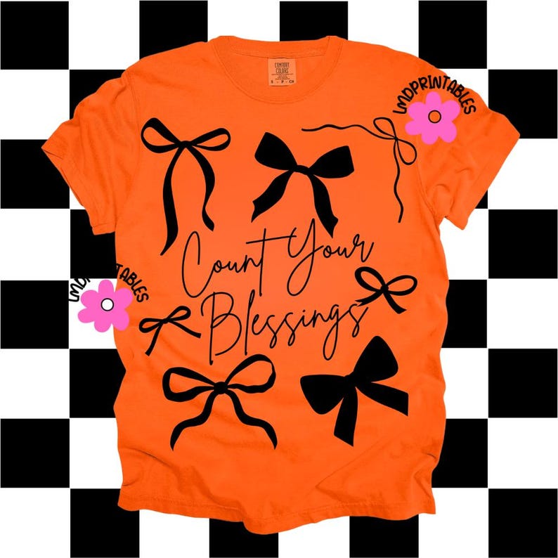 K&ouml;nnte beinhalten: Leuchtend orangefarbenes T-Shirt mit schwarzen Schleifenmotiven und dem Schriftzug "Count Your Blessings" in Schreibschrift. Das Shirt hat auch eine rosa Blumengrafik und den Text "LMDPRINTABLES".