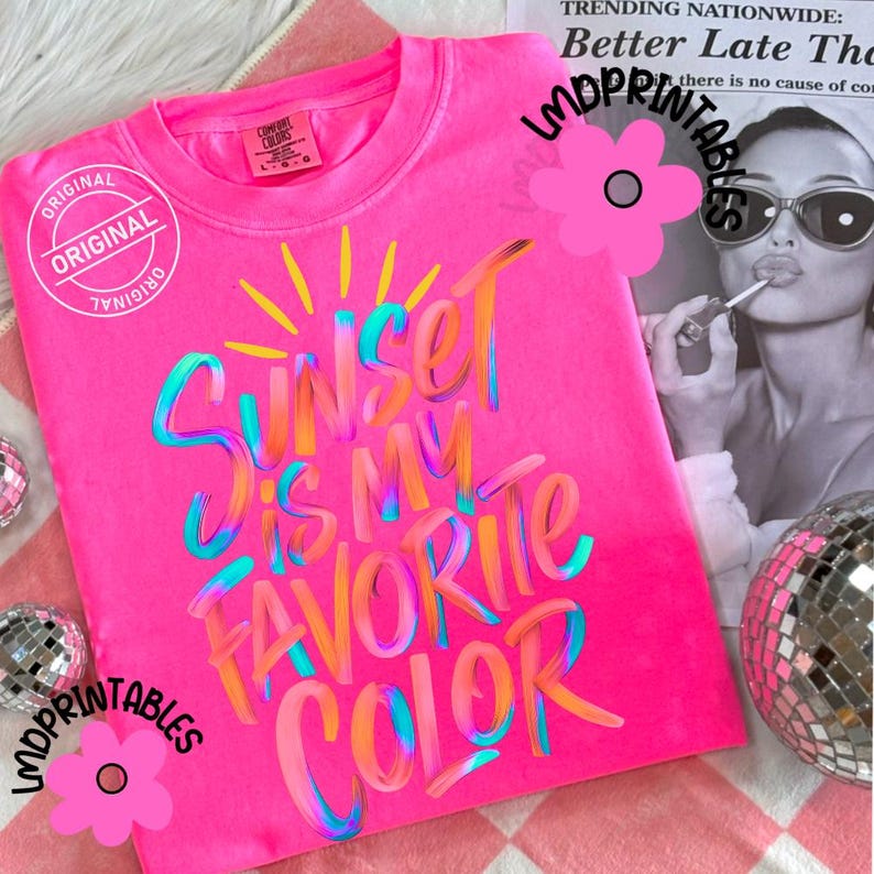 May include: A bright pink t-shirt with the text "Sunset is my favorite color" in colorful, brush-stroke lettering. The shirt has a crew neck and short sleeves. The word "Original" is stamped on the shirt.