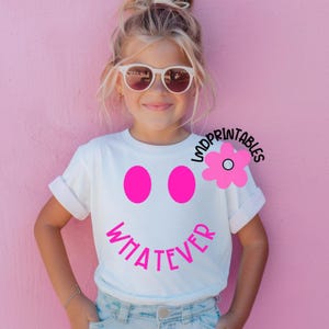 May include: White t-shirt with a pink smiley face design. The design includes two pink circles for eyes and the word "WHATEVER" in pink. A pink flower graphic is on the right side of the shirt.