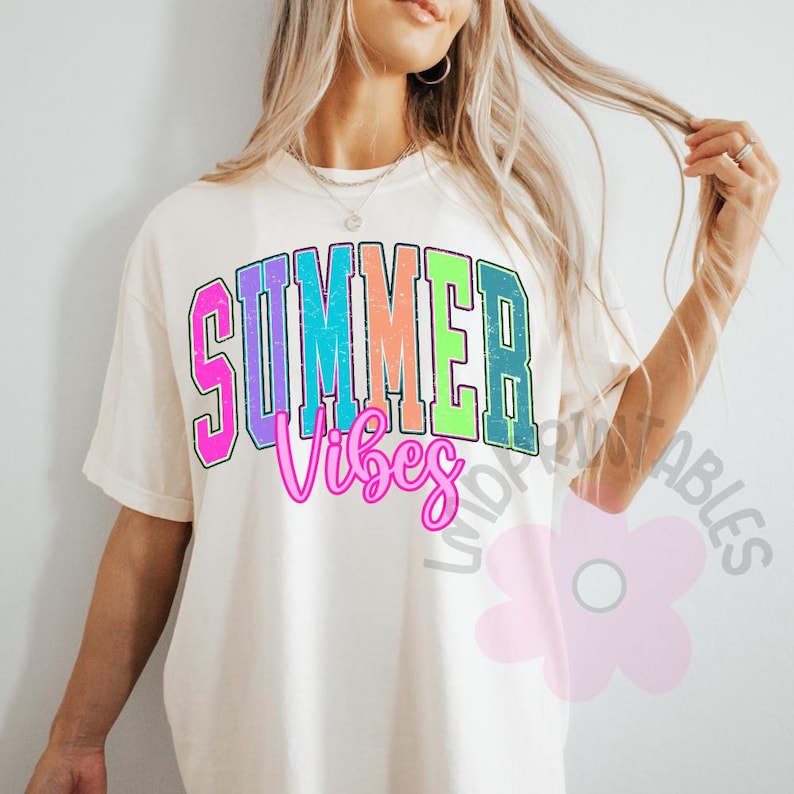 Puede incluir: Camiseta color crema con las palabras "SUMMER Vibes" en una fuente colorida y desgastada. El texto est&aacute; delineado en negro y presenta tonos de rosa, azul, verde y naranja. La camiseta tiene mangas cortas y un corte holgado.