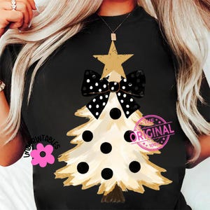 May include: Black t-shirt featuring a Christmas tree design. The tree is cream-colored with black polka dots and a gold star and bow. The shirt has the text "THE ORIGINAL" in a pink stamp.