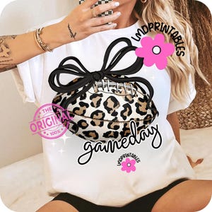 May include: White t-shirt featuring a football with a leopard print design, tied with a black bow. The word "gameday" is written in a cursive font. A pink flower graphic and the text "LMDPRINTABLES" are also visible.