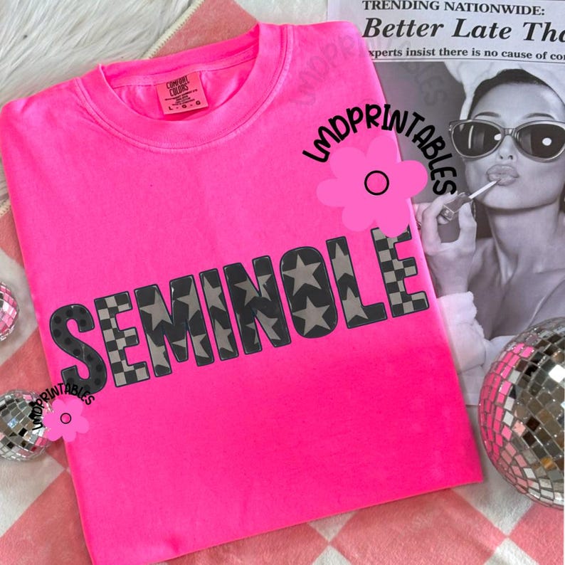 May include: Bright pink sweatshirt with the word "SEMINOLE" in large, gray letters. The letters are patterned with stars and a checkered design. The shirt is on a pink and white checkered surface.