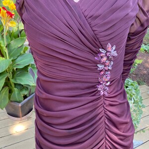May include: A long-sleeved, purple dress with a gathered bodice and a jeweled embellishment on the left side.