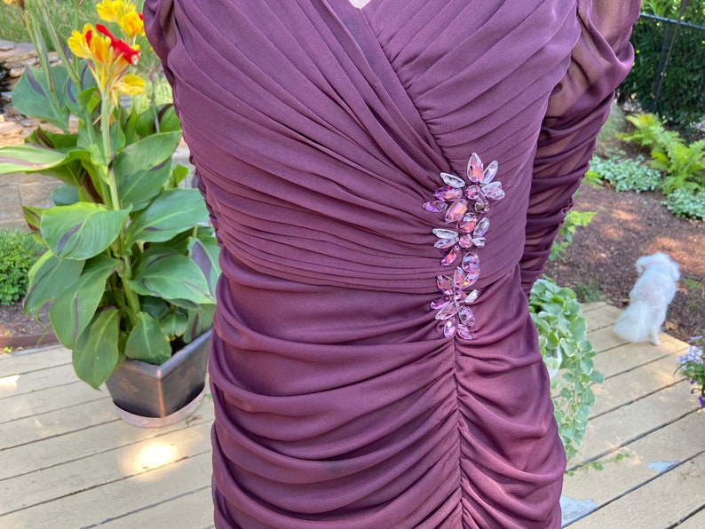 May include: A long-sleeved, purple dress with a gathered bodice and a jeweled embellishment on the left side.