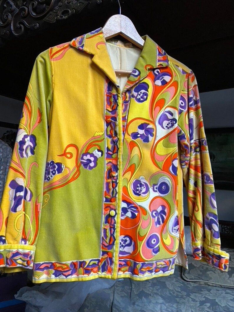 Op de afbeelding: Een lang mouw overhemd met knopen en een psychedelisch patroon in tinten van groen, geel, oranje, paars en wit. Het overhemd heeft een kraag en een knoopsluiting.