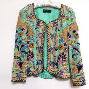 May include: A mint green embroidered jacket with a floral pattern in shades of gold, purple, blue, and black. The jacket has a front closure and long sleeves.