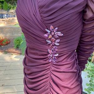 May include: A close-up of a purple dress with a cluster of iridescent rhinestones on the bodice.