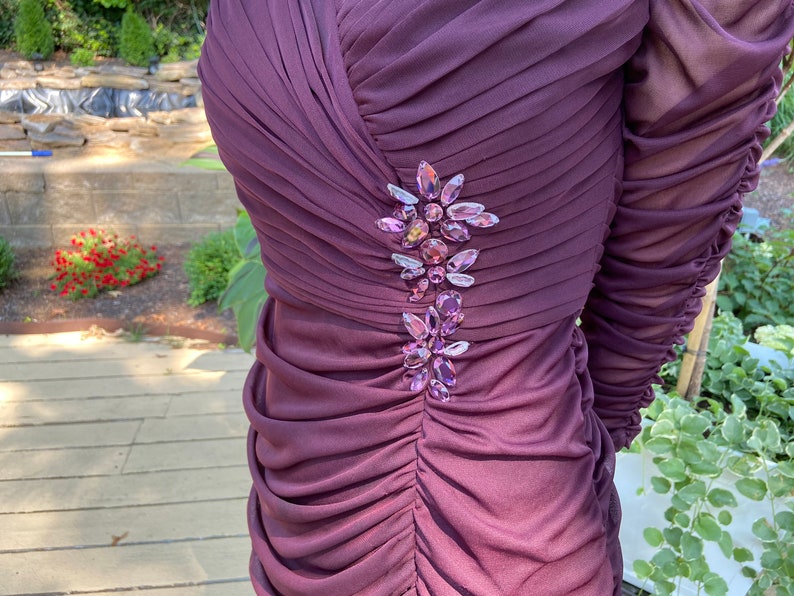 May include: A close-up of a purple dress with a cluster of iridescent rhinestones on the bodice.
