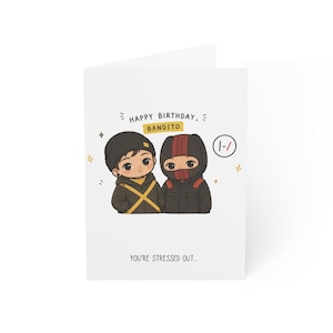 May include: A white greeting card with a cartoon illustration of two figures. One figure wears a black beanie and a yellow cross design, the other wears a black mask with red stripes. Text includes "HAPPY BIRTHDAY, BANDITO" and "YOU'RE STRESSED OUT..."