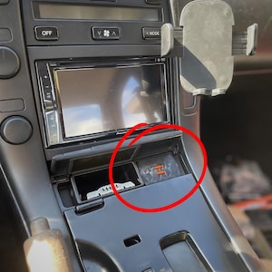 Puede incluir: Panel de instrumentos de coche con un sistema estéreo Pioneer, controles de aire acondicionado y un soporte para teléfono. La consola central tiene un pequeño compartimento con dos puertos USB naranjas para cargar dispositivos.